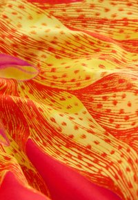 Tissu floral jaune vif et rouge avec des motifs détaillés de pétales et une touche de rose sur un fond lisse et drapé.