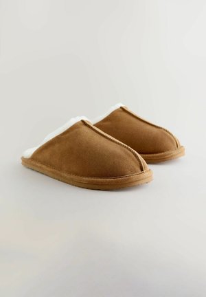 Bruine suède slippers met witte fleece voering, gebogen ontwerp en rubberen zool. Naaddetails zichtbaar langs de randen.
