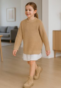 Beige gestrickter Pullover mit Rippenstruktur, kombiniert mit einem weißen Hemdkleid. Tanfarbene Schnürstiefeletten mit einer klobigen Sohle.
