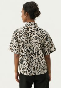 Majica s kratkim rukavima u leopard printu, s bež pozadinom i crnim te smeškim mrljama. Oštri ovratnik i opušteni kroj.