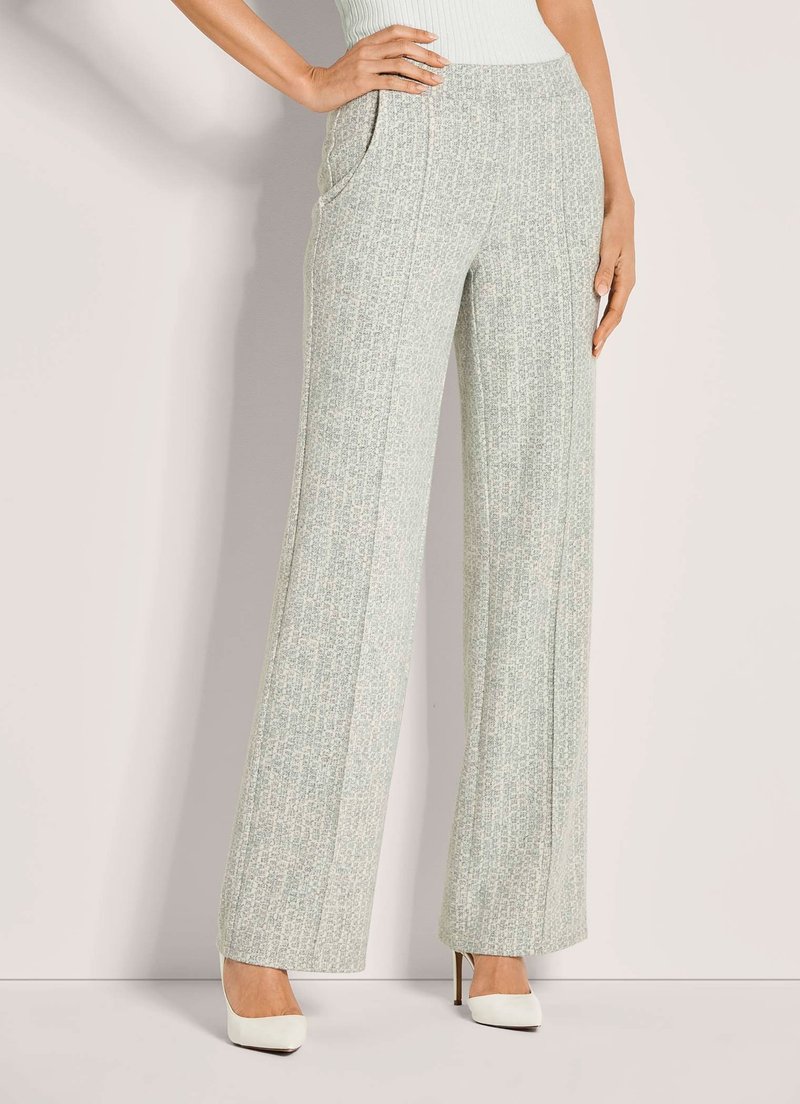 Vrouw in hooggewaisted, wijdvallende lichtgrijze broek met textuur en zakken, gecombineerd met witte puntige hakken en een witte mouwloze top.
