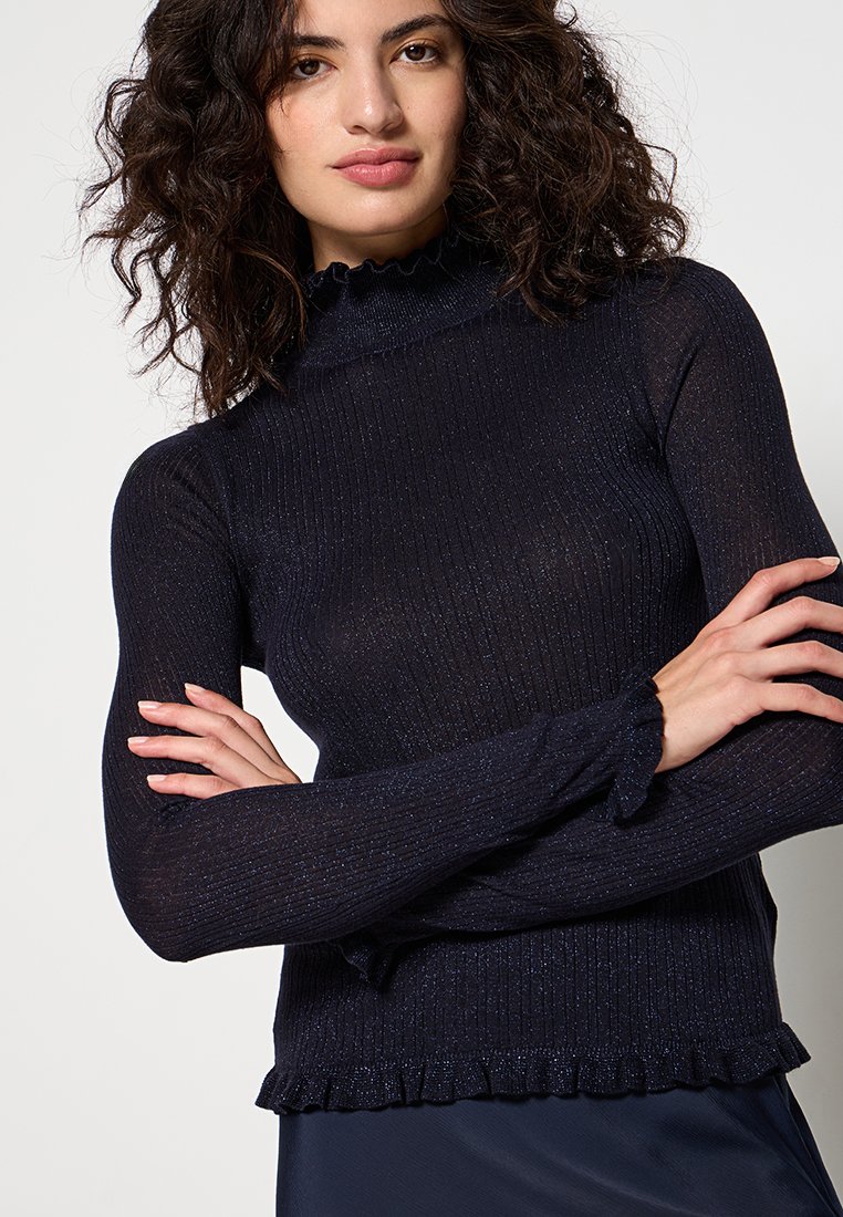 Haut à manches longues bleu marine avec un col montant à volants, des détails métalliques fins et une silhouette ajustée. Texture douce et tissu extensible.