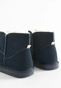 Navy blue suede ankle boots with white fur lining, smooth texture, rounded design, stitched accents, and a black rubber sole.