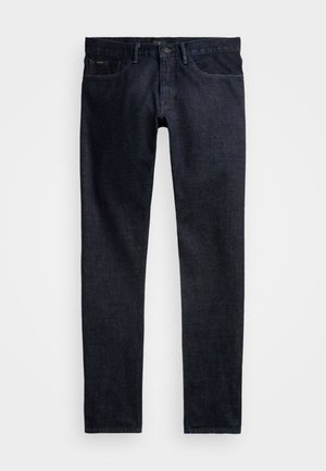 Tumšas džinsa bikses ar pieguļošu piegriezumu, kuras izceļ klasisku piecu kabatu dizainu, jostas cilpas un kontrastējošu šuvju. Nav redzamu bojājumu.