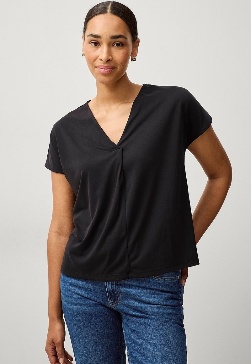 Sort T-shirt med kortærmer og V-udskæring samt samlet detalje i midten, lavet af letvægtigt stof, parret med blå jeans.