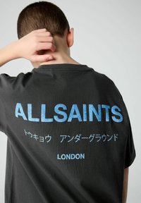 Juodas trumpas rankovėmis marškinėliai su dideliu mėlynu tekstu "ALLSAINTS" ant nugaros, su japonišku raštu ir "LONDON" atspausdintu žemiau.