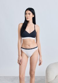 Czarny biustonosz z cienkimi ramiączkami, biała gumka z logo "Tommy Hilfiger"; białe majtki z ciemnym paskiem i logo. Gładkie tło.