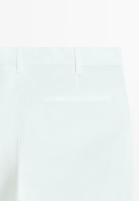 Nærbillede af linningen bagpå og en enkelt paspoleret lomme på et par hvide bukser.