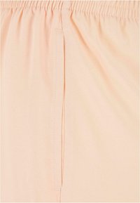 Perzikkleurige stof met een elastische tailleband en een zijdetaile. Glad textuur en lichtgewicht materiaal, geschikt voor casual wear.