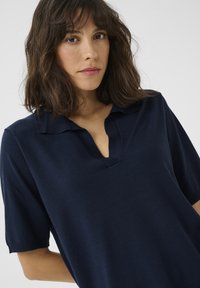 Navyblå kortärmad polo med V-ringning och mjuk, slät textur. Har en minimalistisk design och en vikbar krage.
