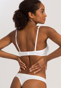 Bílý spodní prádlo set obsahující podprsenku s nastavovacími ramínky a háčkovým zapínáním, doplněný o ladící tanga. Hladká tkanina s minimalistickým designem.