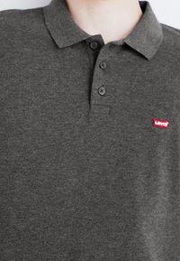 Polo shirt gris foncé en mélange de coton, avec un col, une patte de boutonnage à trois boutons et un petit logo rouge Levi's sur la poitrine.