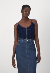 Mornarsko denim kratek top z zadrgo spredaj, tankimi naramnicami in kontrastnim šivanjem, v kombinaciji z visokim denim krilom v podobni barvi.