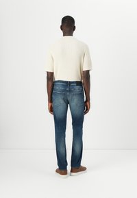 Cămașă scurtă cu mânecă, din tricot ribbed, de culoare bej deschis, asociată cu blugi slim-fit de culoare albastru închis, având o spălare ușor estompată și buzunare la spate.