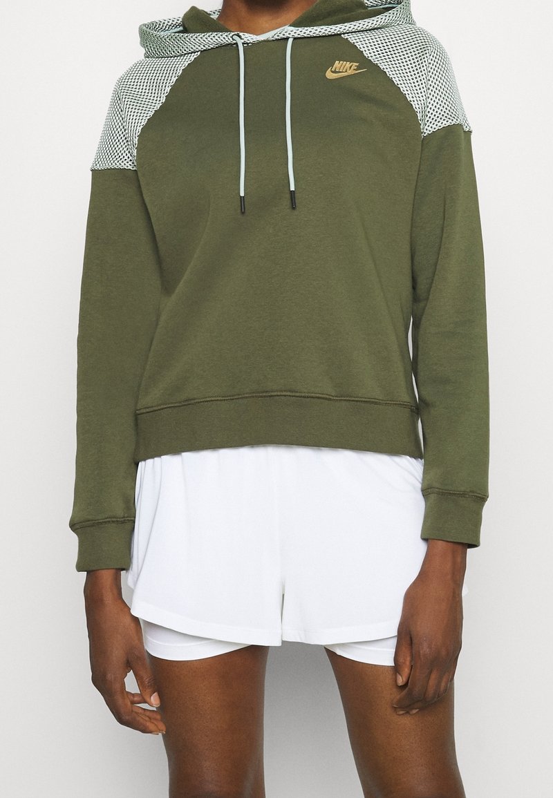 Oliwkowy hoodie z siateczkowym kapturem i yoke, z jasnoniebieskimi sznurkami oraz złotym logo Nike. Wykonany z miękkiego, strukturalnego materiału.
