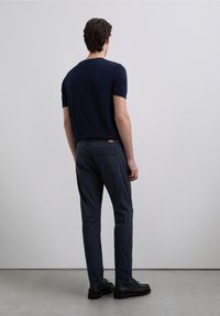 Navy blue short-sleeve t-shirt paired with dark gray pants and black shoes, viewed from the back. Smooth texture, simple design.