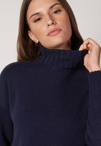 Marineblauer Strickpullover mit einem gerippten Stehkragen, strukturiertem Stoff und langen Ärmeln. Das Design bietet eine lockere Passform und dezente Stichdetails.