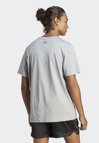 Šedé bavlněné tričko s volným střihem, krátkými rukávy a bezšvovým límcem vzadu, na kterém je v horní části malé černé logo Adidas.