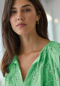 Blusa verde ricamata con motivi floreali, caratterizzata da un collo a V e maniche fluide. Il tessuto ha un aspetto leggero e testurizzato.