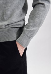 Pull gris tricoté avec poignets et ourlet côtelés, associé à un pantalon noir. La texture semble douce et la coupe est ajustée au corps.