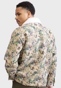 Giubbotto di jeans con motivo floreale, caratterizzato da uno sfondo crema con accenti verdi e blu, e un morbido colletto in shearling bianco.