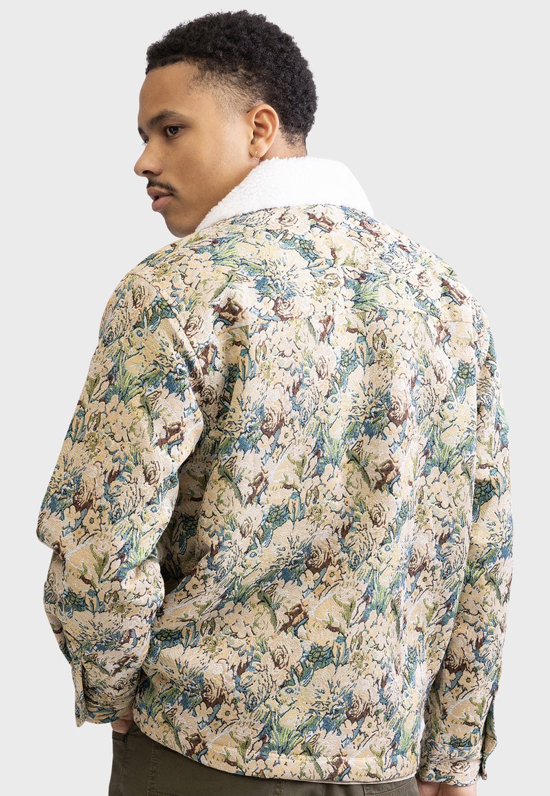 Giubbotto di jeans con motivo floreale, caratterizzato da uno sfondo crema con accenti verdi e blu, e un morbido colletto in shearling bianco.
