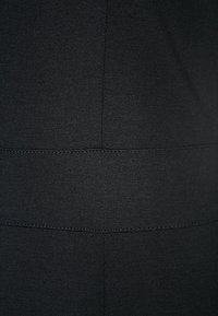 Gros plan sur un tissu noir avec des coutures horizontales et verticales formant un motif géométrique simple.
