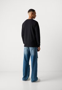 Sort langærmet skjorte med rund halsudskæring, parret med lyseblå denim jeans med slidte detaljer. Model vender væk.