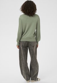 Pulover verde cu dungi și mâneci bufante, asortat cu blugi gri cu picioare largi, cusături contrastante și buzunare în spate, plus adidași albi.