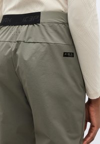 Τα γκρι παντελόνια διαθέτουν φαρδύ ζωνάρι με σκούρες λεπτομέρειες, υφή υφάσματος, ένα αυτοκόλλητο με το κείμενο "A.W.S. EXTREME" και διακοσμητικές τρυπητές λεπτομέρειες για αερισμό.