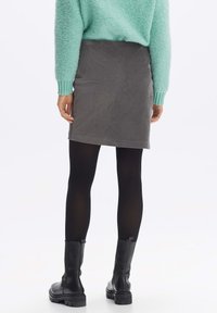 Grauer Hahnentrittrock mit geradem Schnitt, kombiniert mit schwarzen Strumpfhosen und schwarzen klobigen Stiefeln. Hellblauer, flauschiger Pullover mit geripptem Bund.