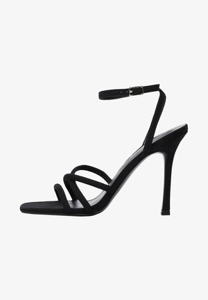 Sandales à talons hauts en suede noir avec des brides fines, une boucle à la cheville et un bout pointu avec une texture lisse. Talons d'environ 10 cm.