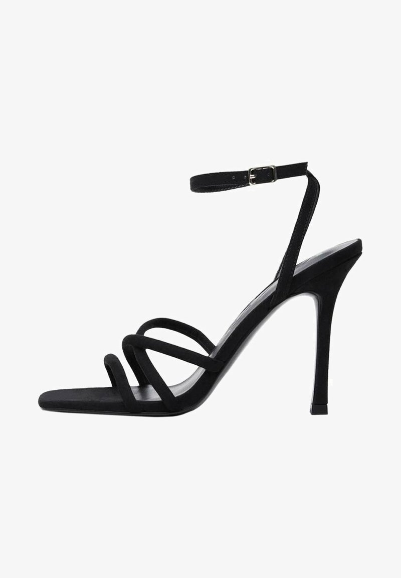 Sandales à talons hauts en suede noir avec des brides fines, une boucle à la cheville et un bout pointu avec une texture lisse. Talons d'environ 10 cm.