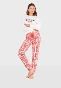 Sudadera blanca con gráfico azul y rojo de "The Beatles"; pantalones de pijama rojos con un patrón repetido de texto en blanco de "The Beatles".