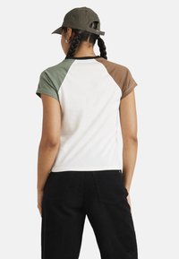 Short-sleeve t-shirt with a white body, green and brown raglan sleeves. Cotton material, slightly fitted, paired with black corduroy pants.
