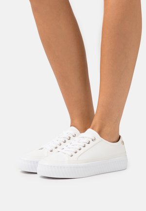 Sneakers bianchi in tela con profilo basso, occhielli metallici e suola in gomma testurizzata. Presentano un design semplice con lacci.