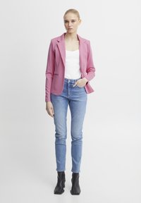 Roze getailleerde blazer over een witte top, gecombineerd met lichtblauwe skinny jeans en zwarte enkellaarsjes. Glad stof, op maat gemaakt ontwerp.