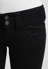 Černé džíny z denimu s přiléhavým střihem, dvěma stříbrnými knoflíky v pase a předními kapsami s jemnými šicími detaily.