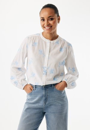 Hvid langærmet skjorte med lyseblå blomsterbroderi, rund halsudskæring, knaplukning foran og opsmøgede manchetter. Kombineret med blå jeans.