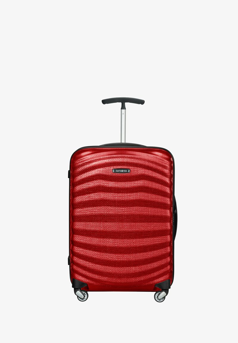 Roter Hartschalenkoffer mit welliger Textur, teleskopischem Griff und vier Rollen für Mobilität. Markenlogo an der Vorderseite sichtbar.