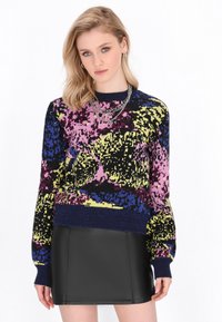 Maglione colorato lavorato a maglia con un motivo grafico in viola, rosa, blu e giallo, accentuato da un colletto e polsini a coste di colore blu navy. Abbinato a una mini gonna nera.