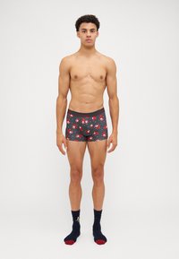 Graue Boxershorts mit einem rot-weißen Muster von Cartoonfiguren. Der Bund ist schwarz mit dem Markennamen in rot. Tragen Sie sie mit dunklen Socken.
