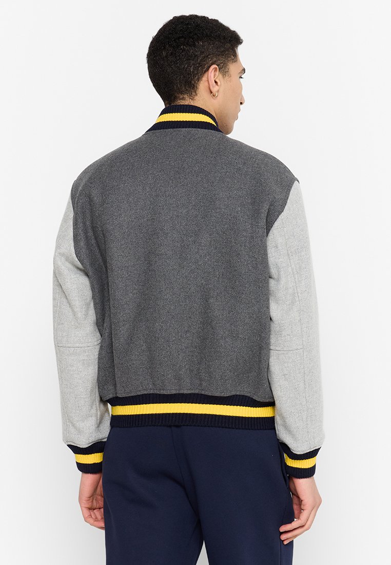 Veste bomber grise et gris clair avec un col côtelé, des accents de rayures jaune et bleu marine, et un tissu texturé. Présente des poignets et un ourlet ajustés.
