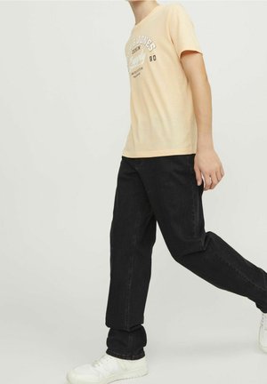 T-shirt pêche clair avec imprimé graphique blanc, associé à un jean noir foncé et des baskets blanches. Tenue simple et décontractée aux couleurs contrastées.