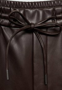 Pantalon en cuir marron avec une taille élastique et un cordon de serrage noué. Le matériau présente une texture lisse et des coutures espacées avec un éclat subtil.