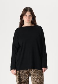 Black knit sweater with a boxy fit, wide neckline, and long sleeves, paired with patterned leopard pants. Soft texture and subtle stripe detail.