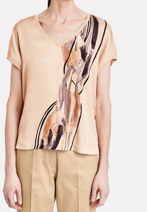 Persikkavärinen V-pääntie paita lyhyillä hihoilla, jossa on monivärinen abstrakti kuvio ruskean, mustan ja vaaleanpunaisen sävyissä yhdellä sivulla.