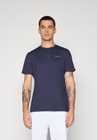Sötétkék, rövid ujjú póló, puha anyagból készült, kerek nyakkal és egy kis fehér Calvin Klein logóval a bal melle részén.