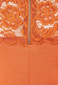 Spetskorsett med blommönster i orange och en silverdragkedja i mitten. Enhetligt orange tyg under, med en mjuk textur.