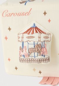 Ύφασμα κρέμα με τη φράση «Carousel» διαθέτει κεντημένο έμβλημα καρουζέλ σε απαλούς τόνους, που δείχνει άλογα και μια ριγέ τέντα με ροζ λεπτομέρειες.
